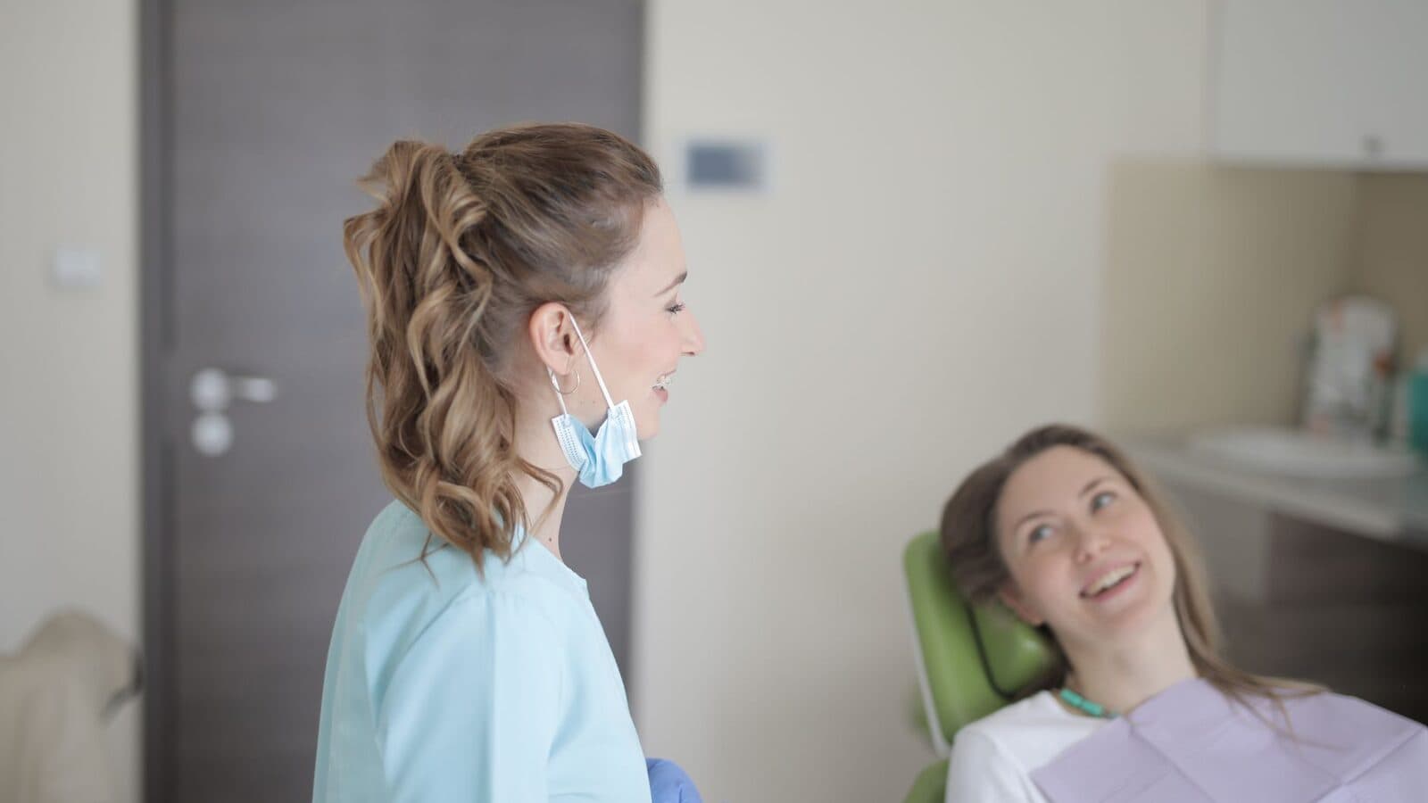 A dentist smiling and talking with a patient seated in the chair